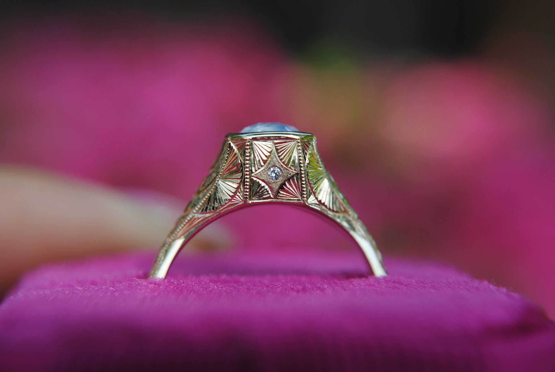 Gold ring with gemstone on a pink cushion against a blurred pink background