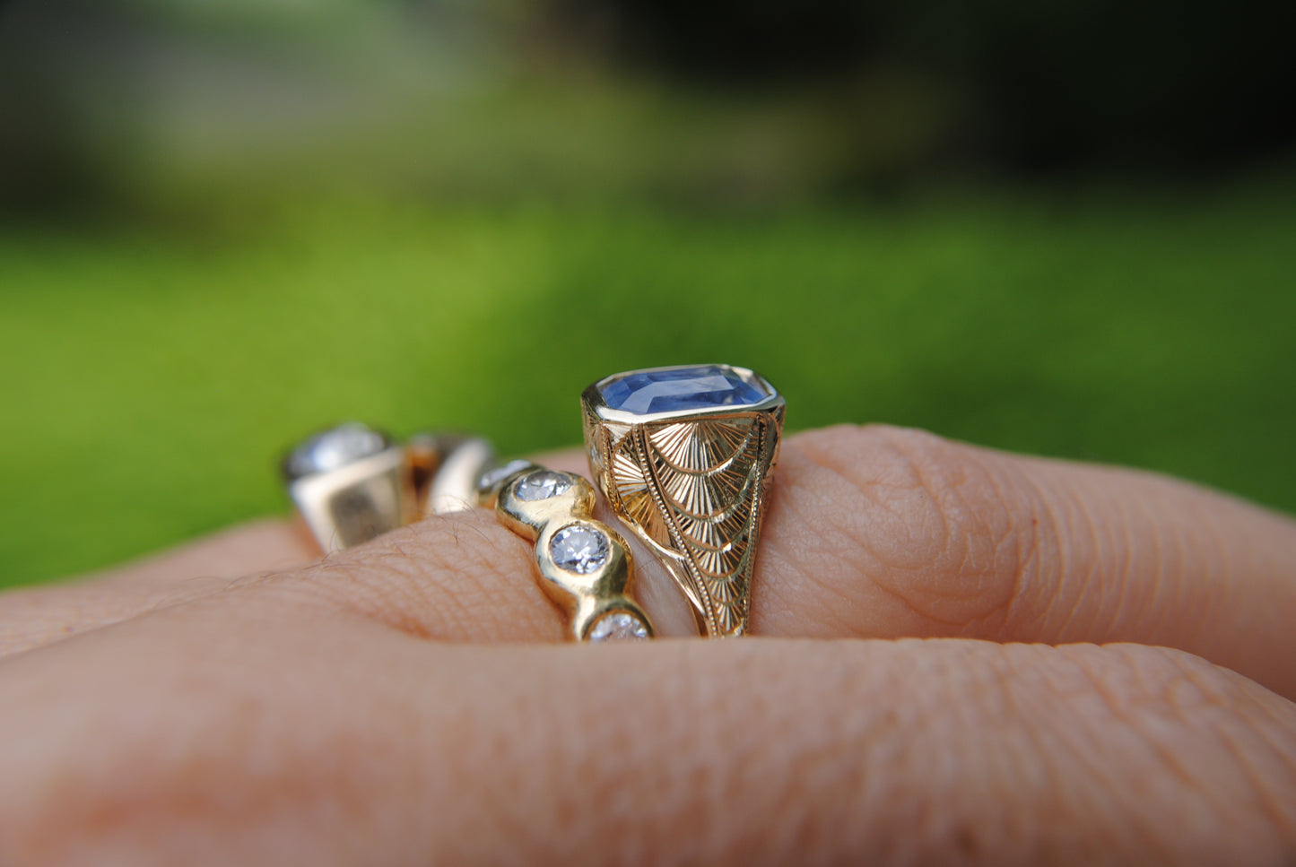Gold ring with gemstones on a hand against a blurred green background