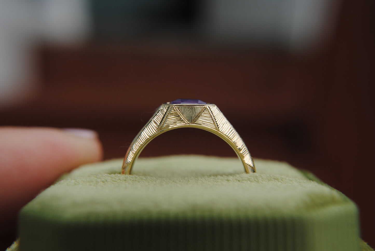 Gold ring with a purple stone on a green cushion, blurred background