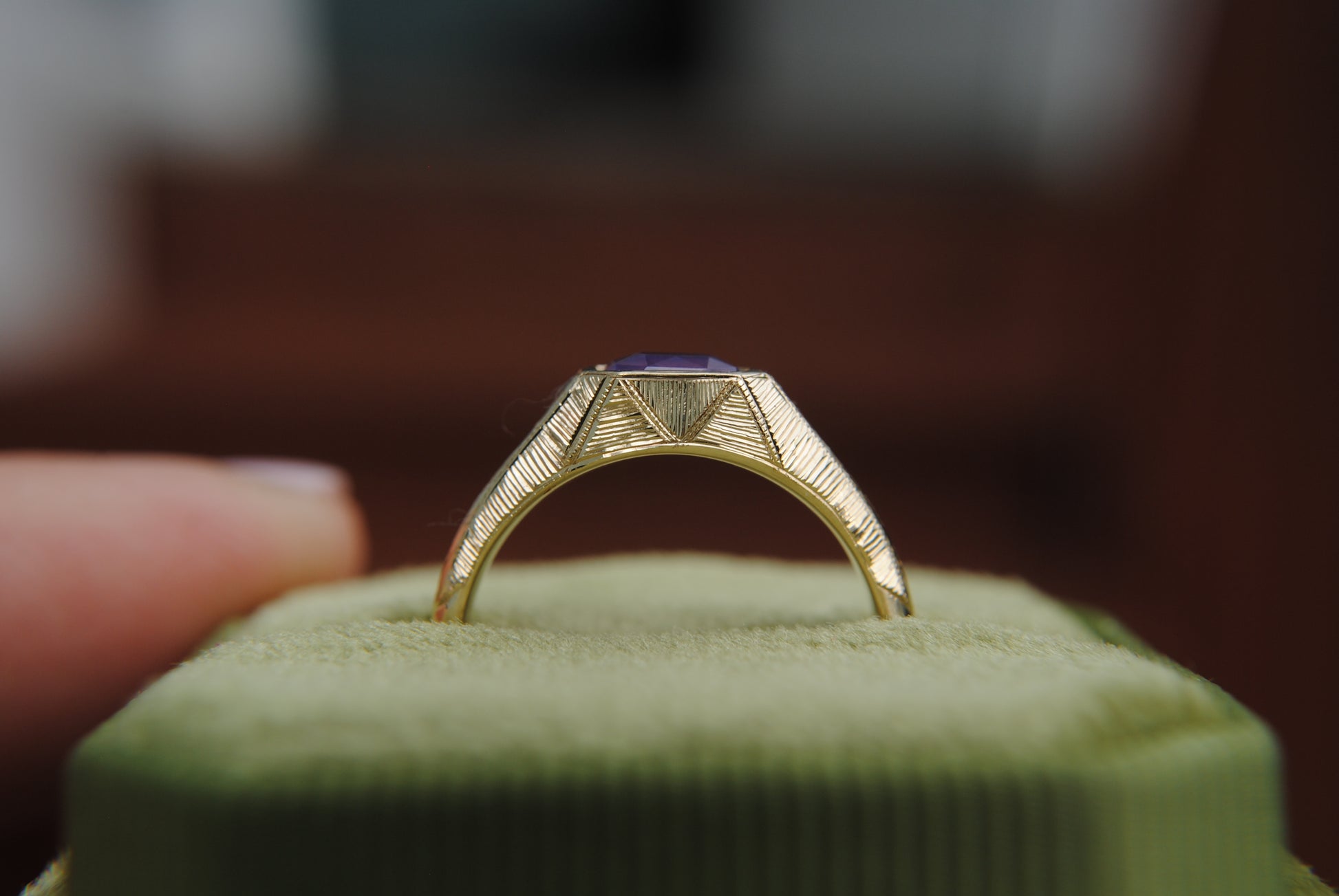 Gold ring with a purple stone on a green cushion, blurred background