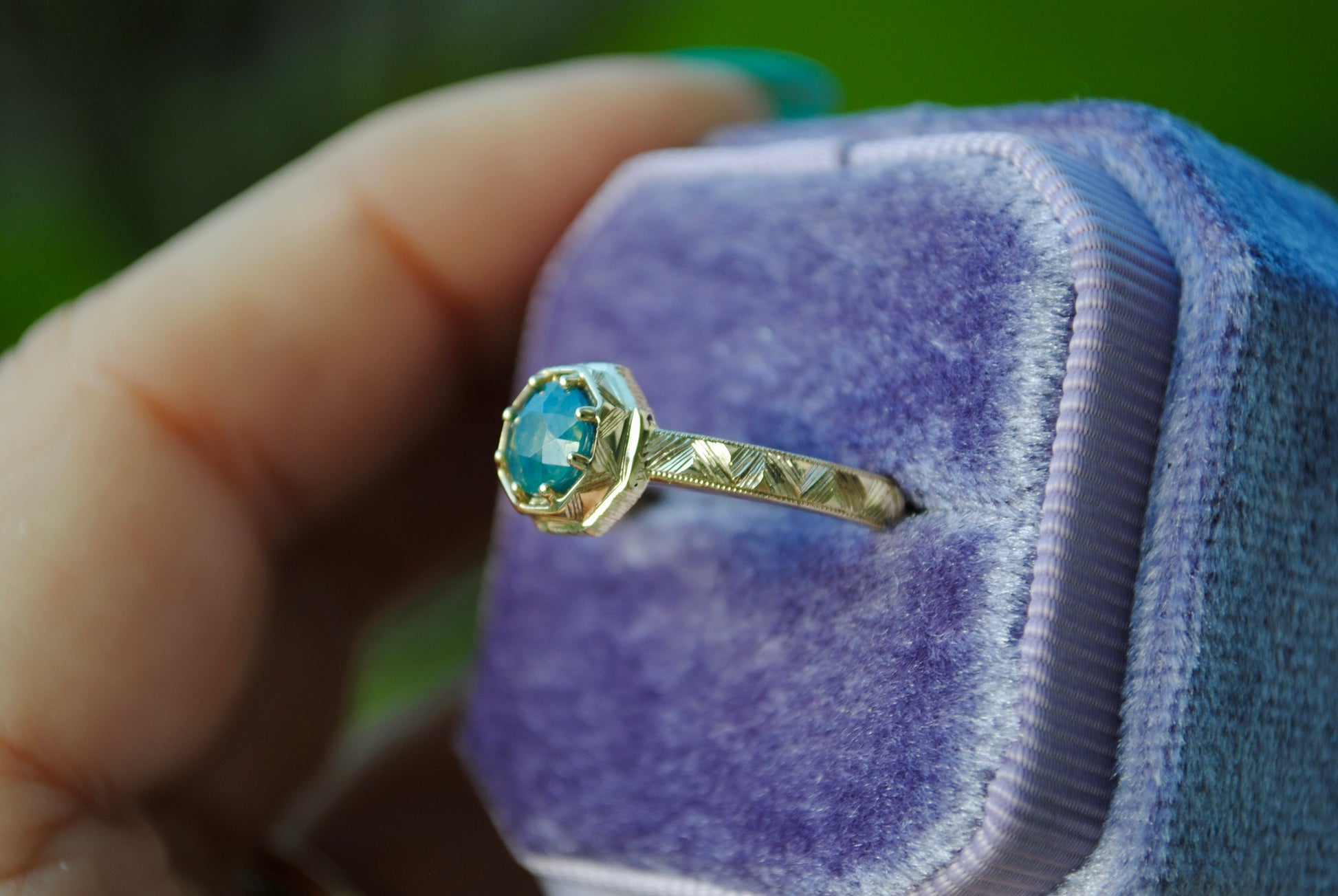 Gold ring with a blue gemstone in a purple jewelry box held by a hand.