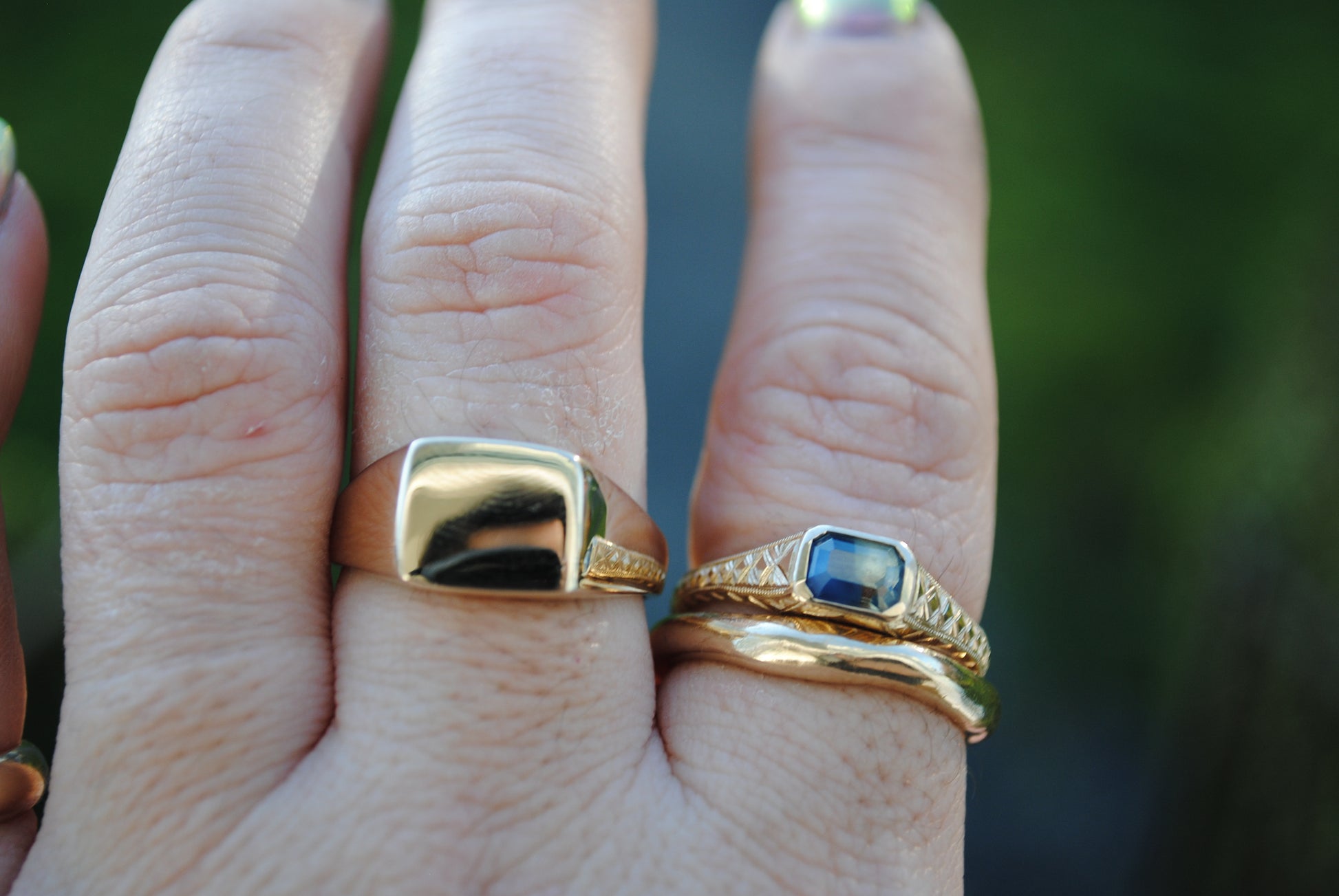 Close-up of a hand wearing two gold rings with a blurred green background