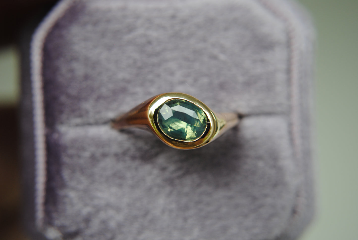 Gold ring with a green gemstone on a gray cushion