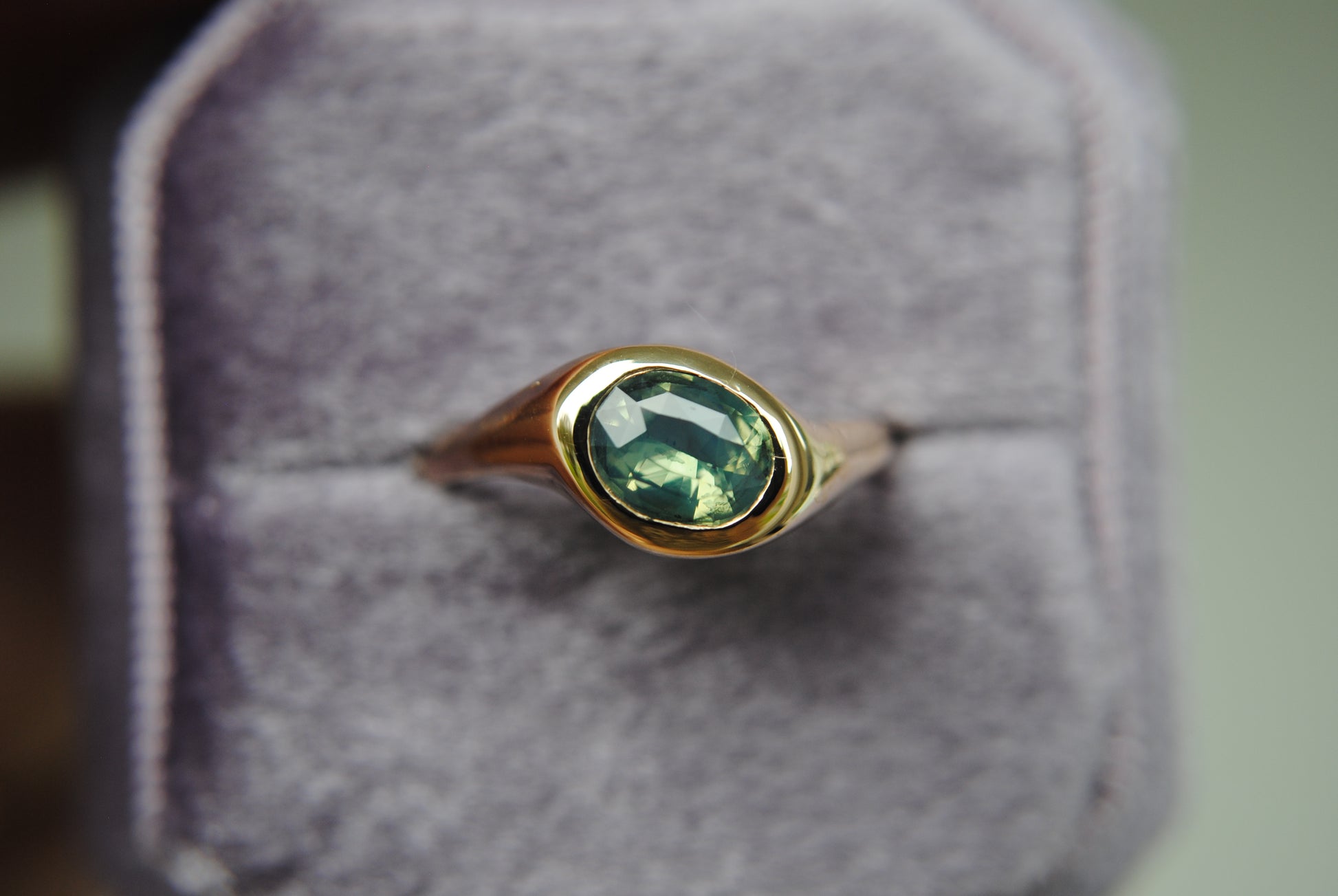 Gold ring with a green gemstone on a gray cushion