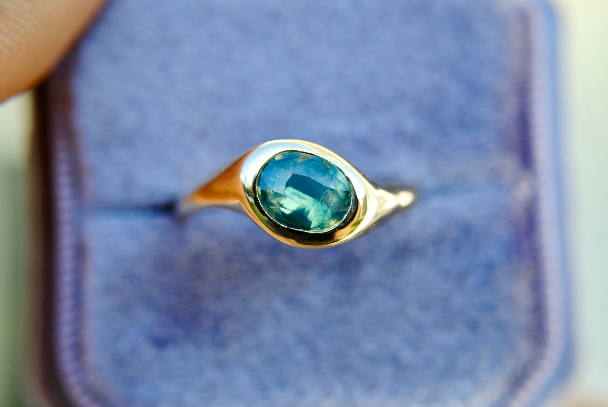 Gold ring with a green gemstone held against a blue background