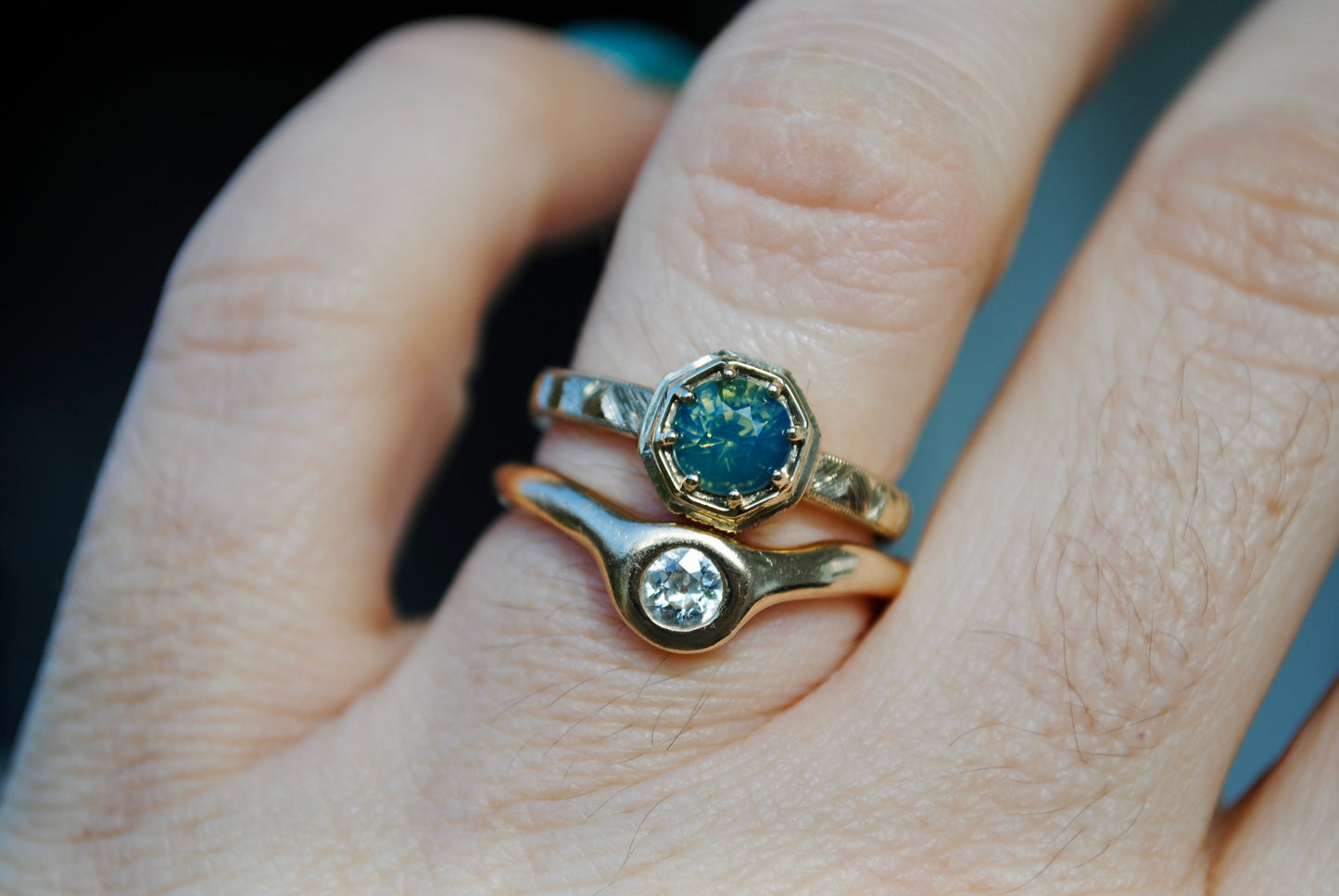 Close-up of a hand wearing two gold rings with gemstones on a blurred background