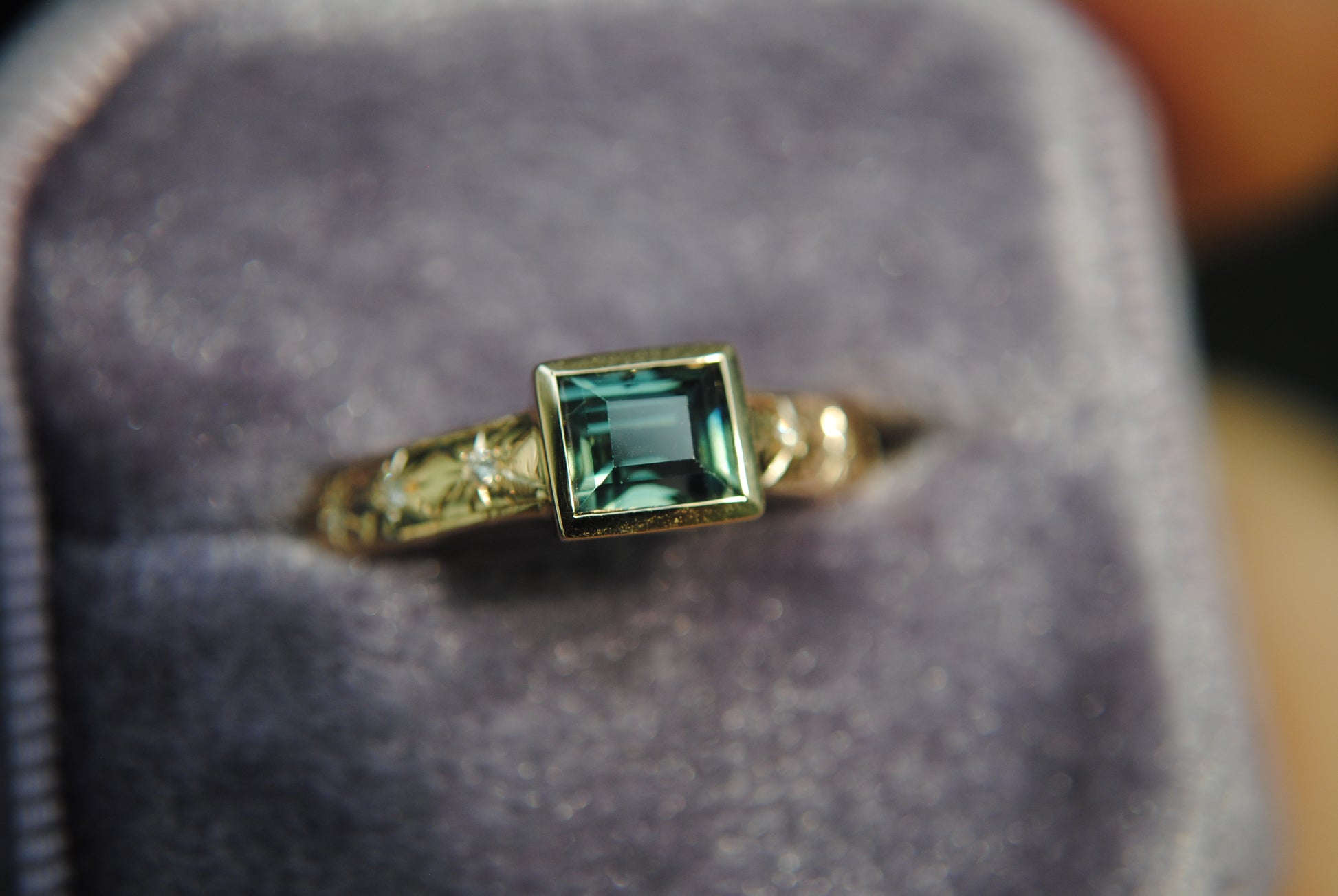 Gold ring with a green gemstone on a gray cushion
