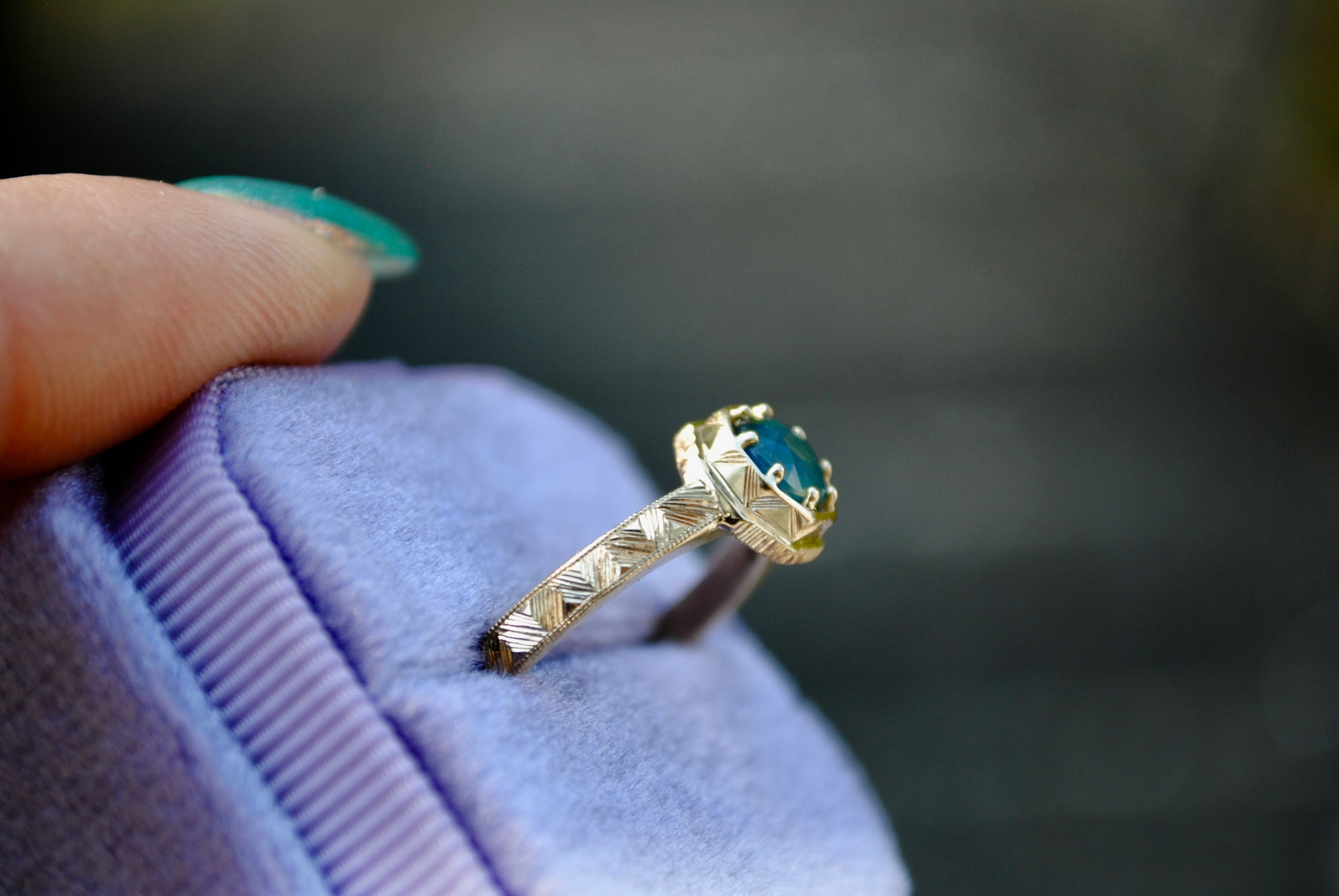 Gold ring with a blue gemstone held on a purple cushion against a blurred background