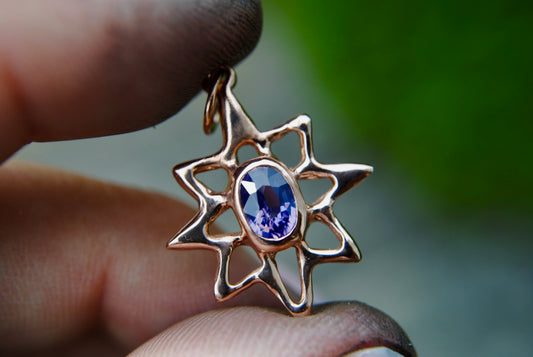 star charm with purple gemstone held between 2 fingers against a blurred background