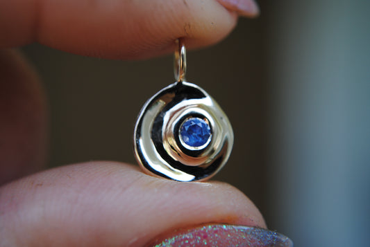 Gold pendant with a blue gemstone held between fingers against a blurred background