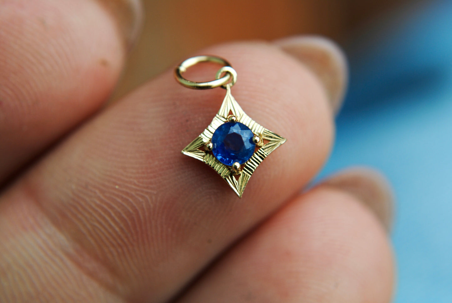 Gold pendant with a blue gemstone held between fingers
