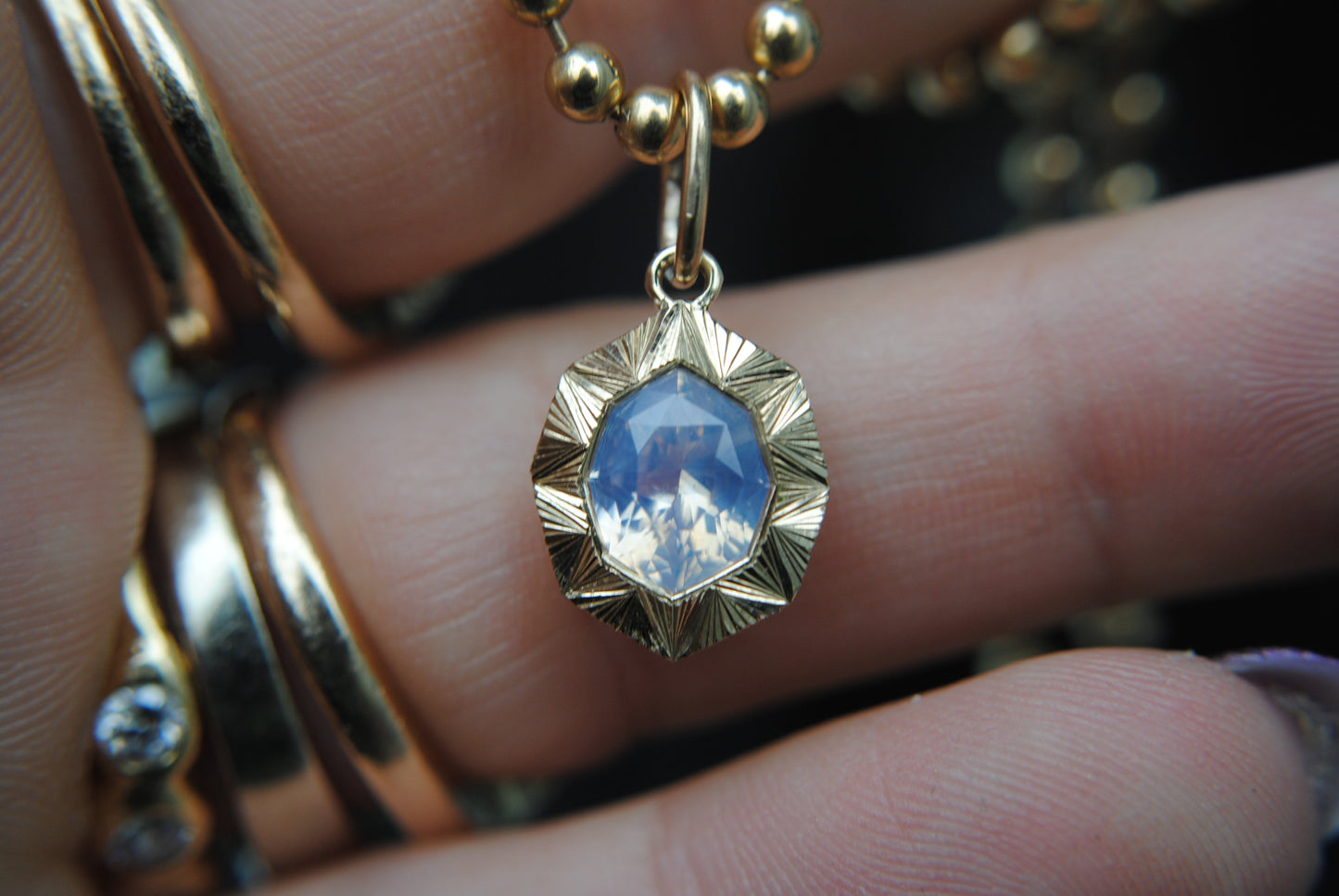 Gold pendant with a blue stone held between fingers