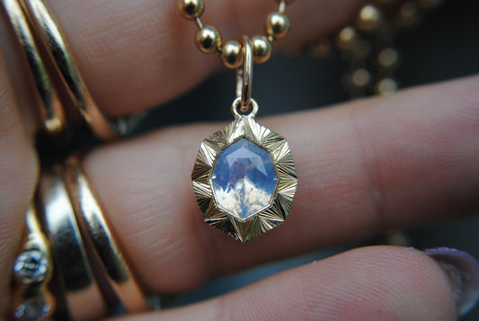 Gold pendant with a blue stone held between fingers