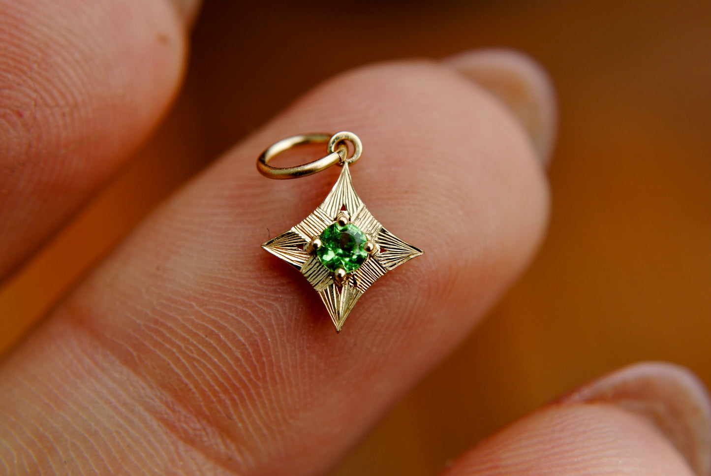 Gold pendant with a green gemstone held between fingers against a blurred background