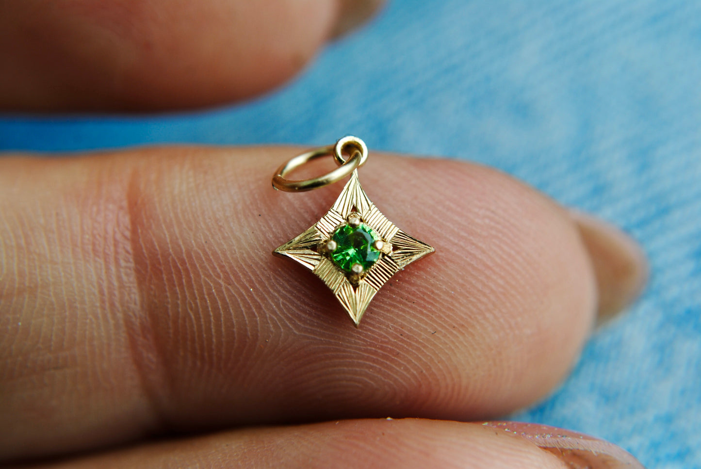 Gold pendant with a green gemstone held between fingers against a blue background
