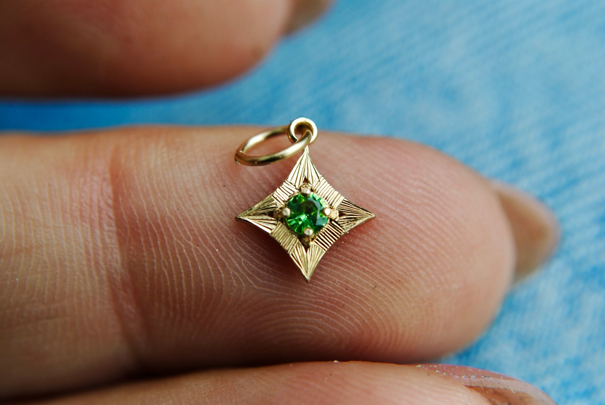 Gold pendant with a green gemstone held between fingers against a blue background