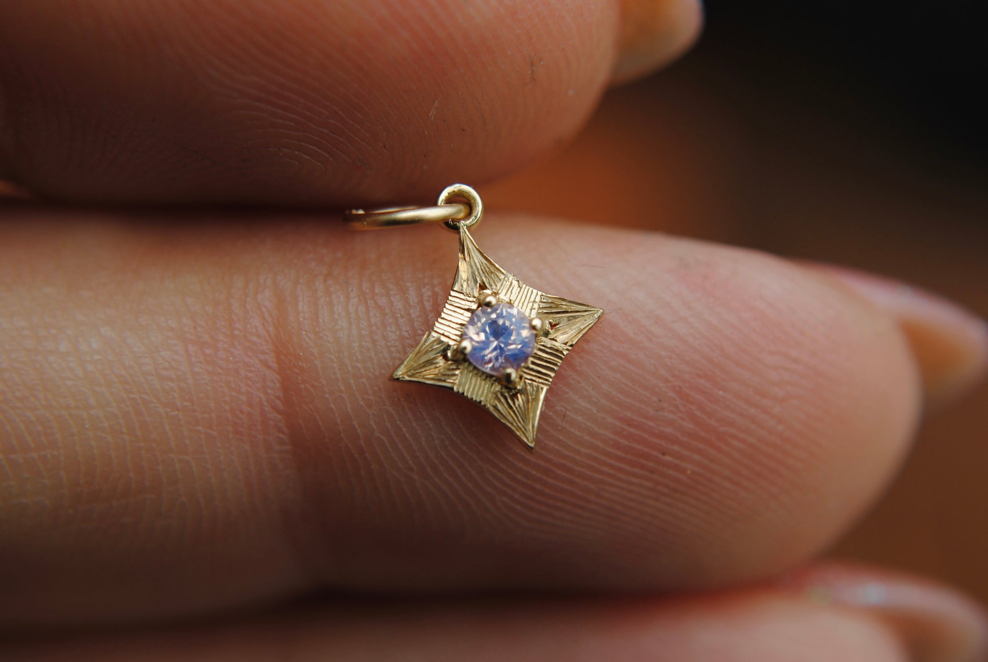 Gold star-shaped pendant with a blue gemstone held between fingers