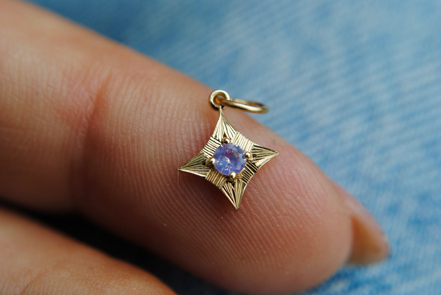 Gold star-shaped pendant with a purple gemstone held between fingers against a blue denim background