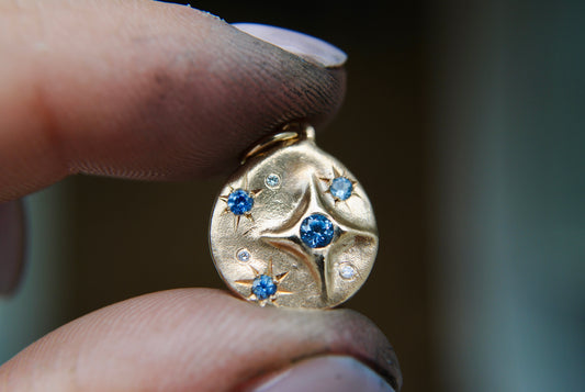 Sapphire charm with stars held between 2 fingers with a blurry background 