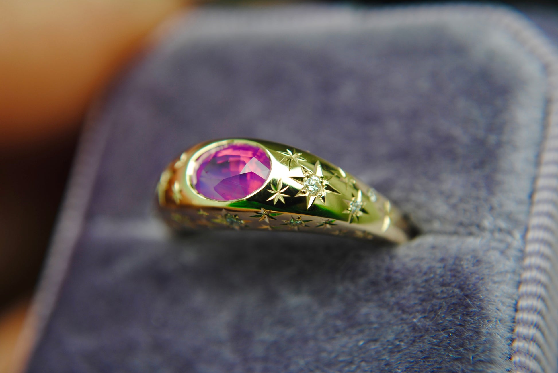 Gold ring with a purple gemstone on a purple cushion