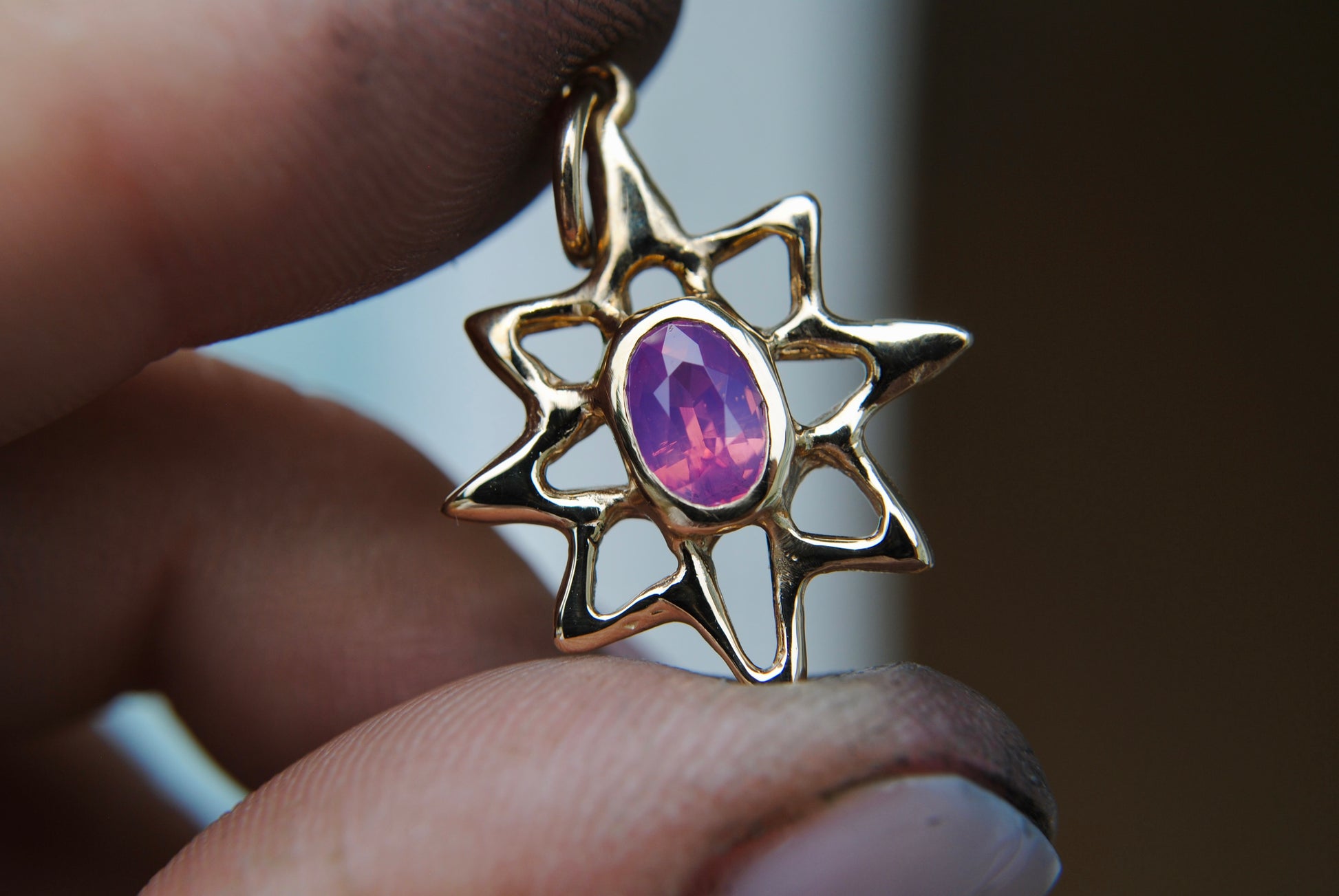 Gold star-shaped pendant with a pink gemstone held between fingers against a blurred background