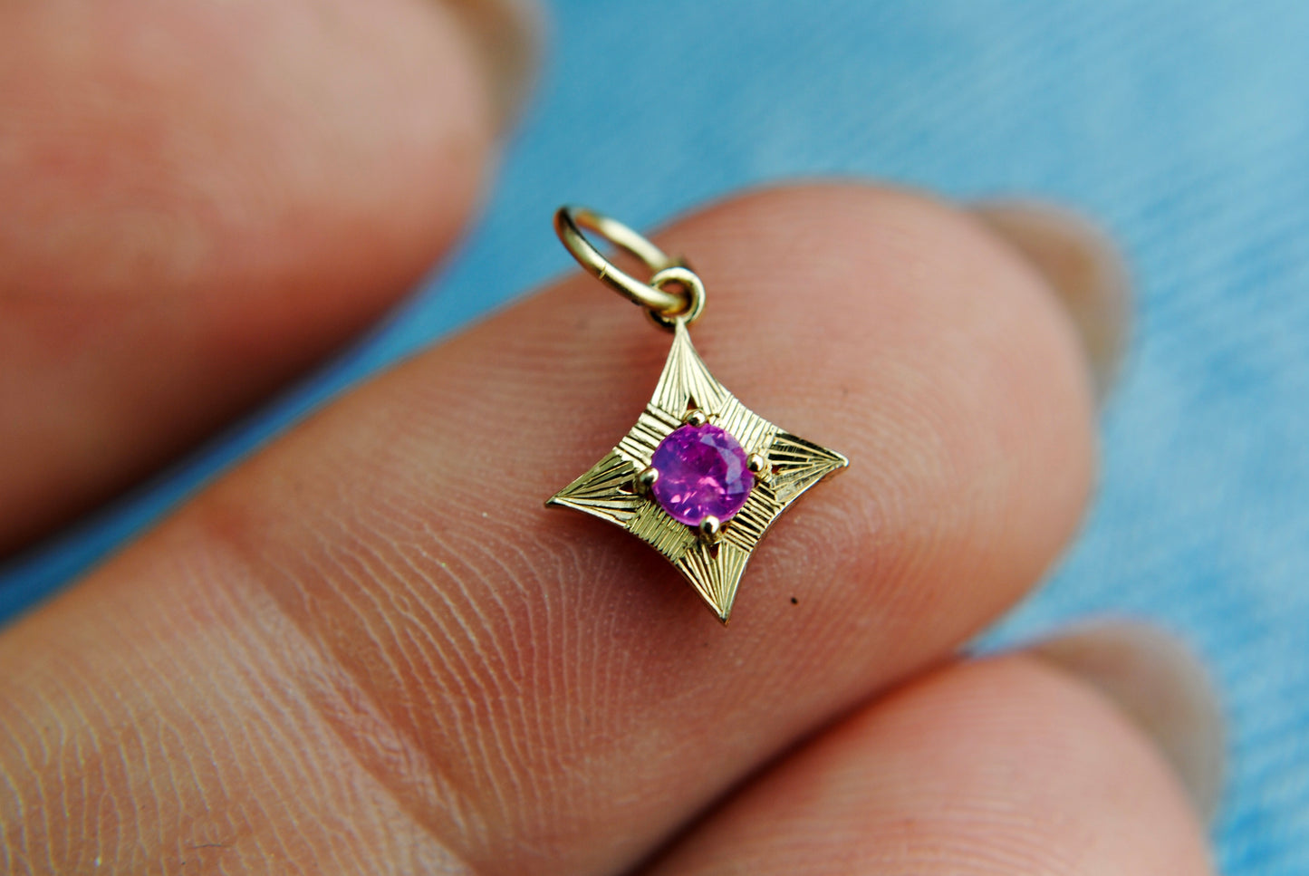 Gold pendant with a purple gemstone held between fingers against a blue background