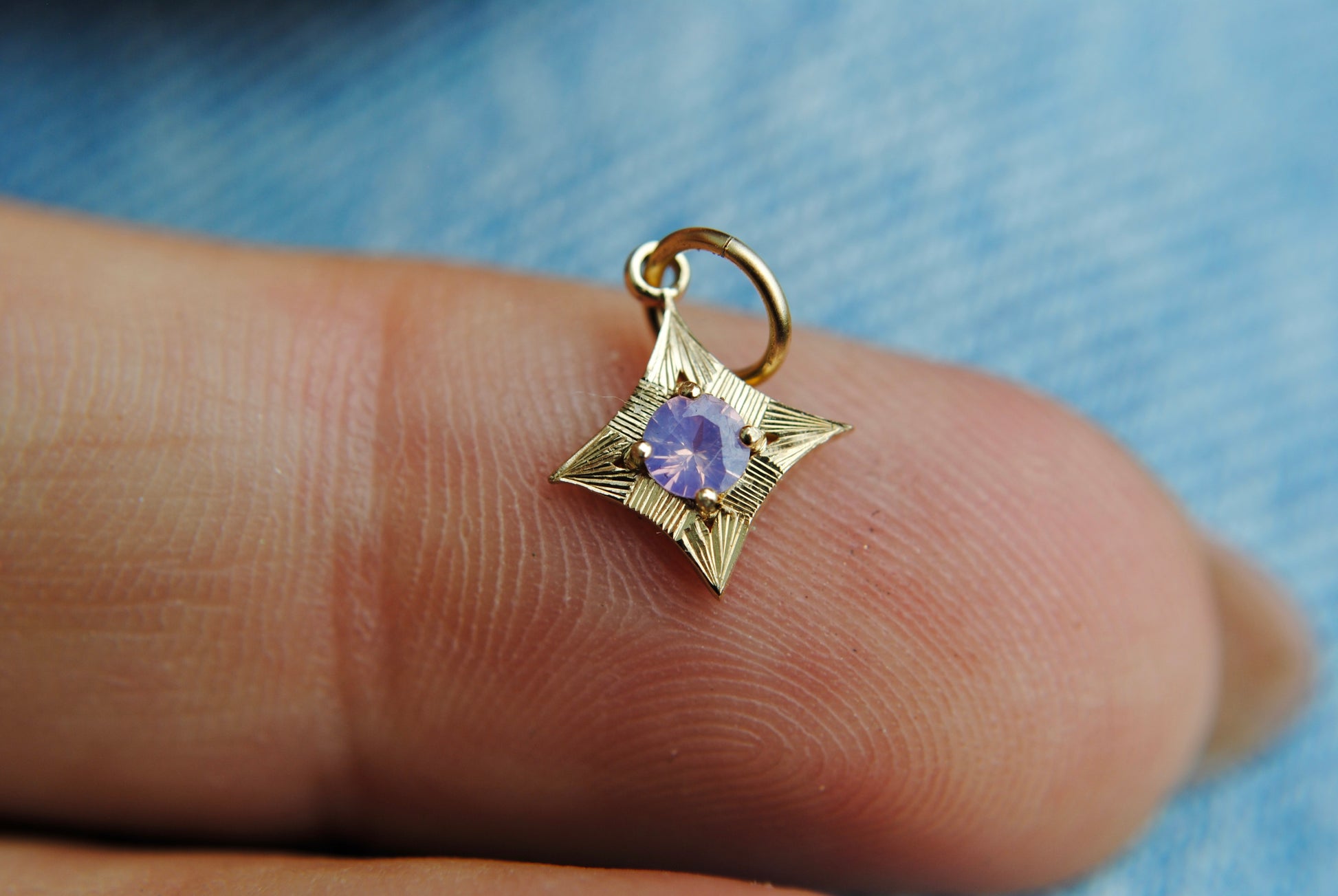 Gold star-shaped pendant with a purple gemstone on a finger against a blue fabric background
