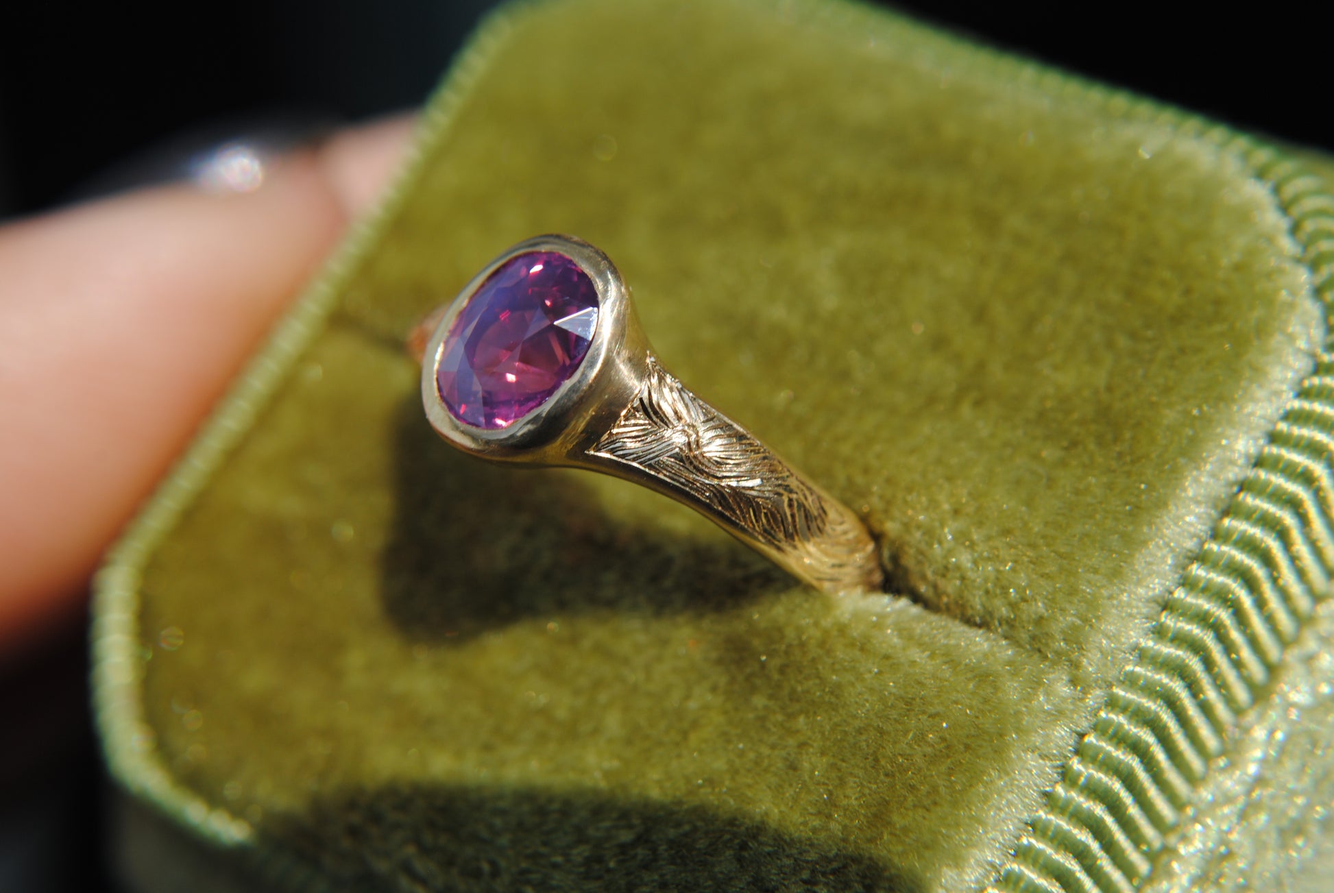 Gold ring with a red gemstone on a green velvet cushion