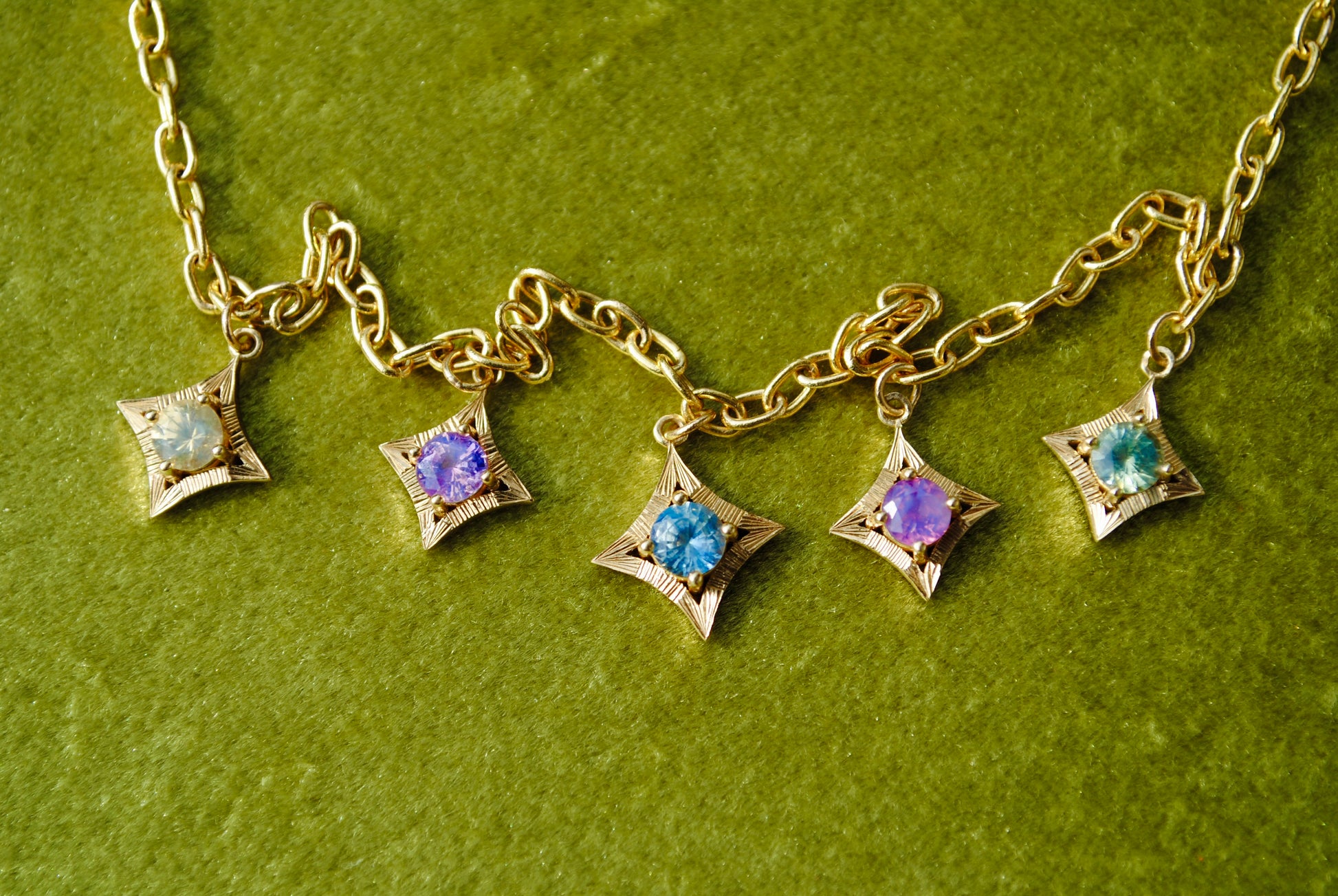 Gold necklace with star-shaped charms featuring colorful gemstones on a green background