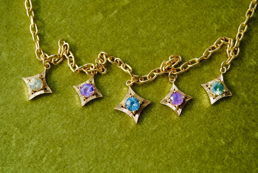 Gold necklace with star-shaped charms featuring colorful gemstones on a green background