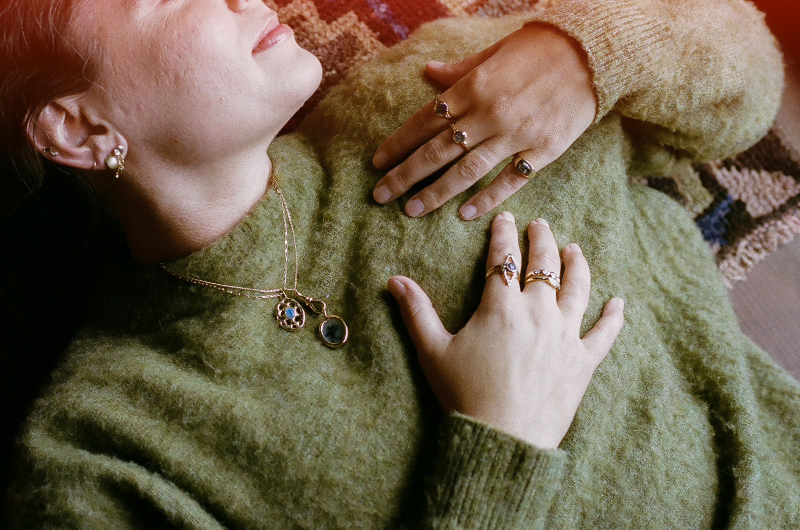 model is wearing a green sweater and decked out in gold jewelry. earrings, necklaces, and rings. 