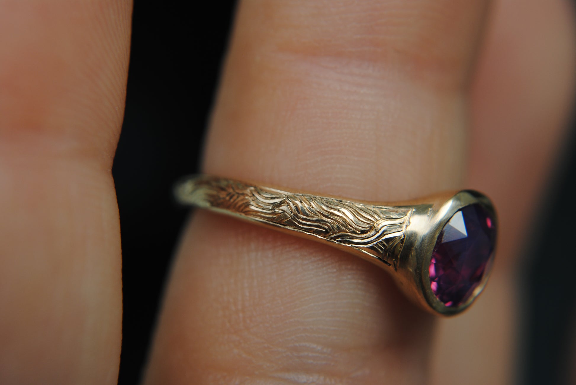 Gold ring with a purple gemstone on a finger against a blurred background
