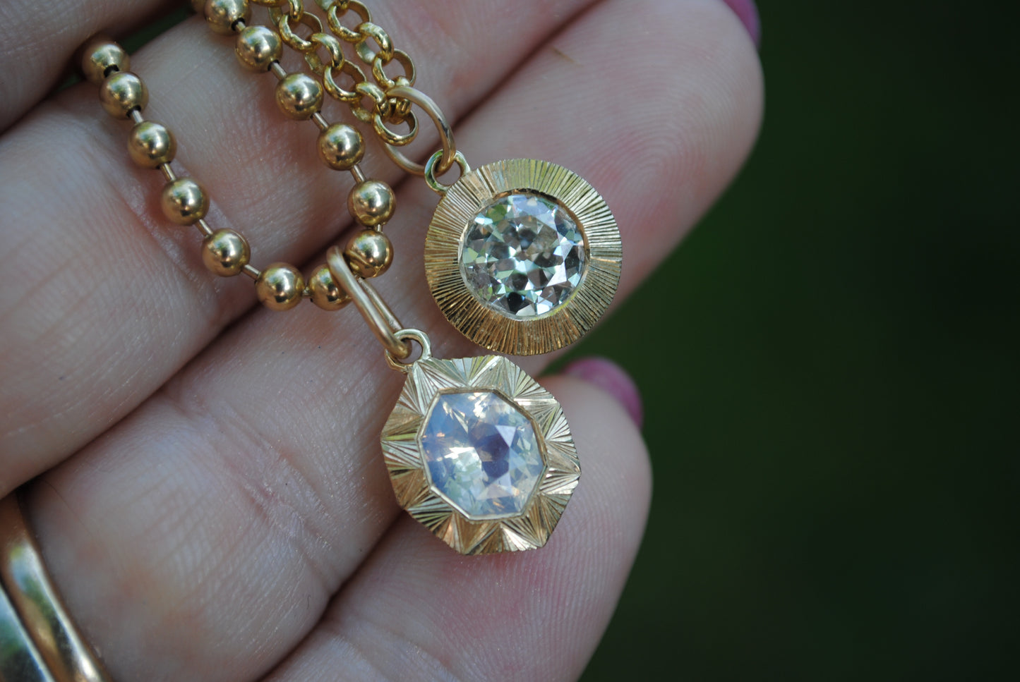 Gold necklace with two pendants held in a hand against a dark background